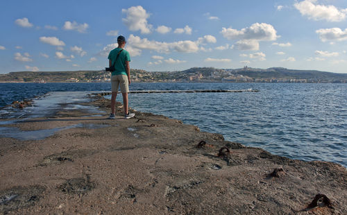 Rear view of man standing on beach against sky