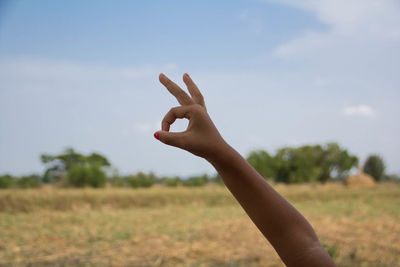 Midsection of person hand on field against sky