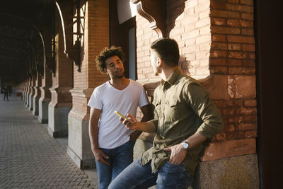 Young multiracial men talking near wall on footpath