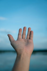 Close-up of hand gesturing against blue sky