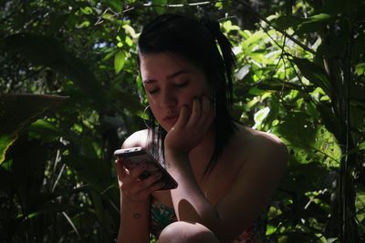 Close-up of young woman using mobile phone against trees