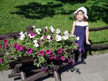 Portrait of girl standing by flowers at park on sunny day