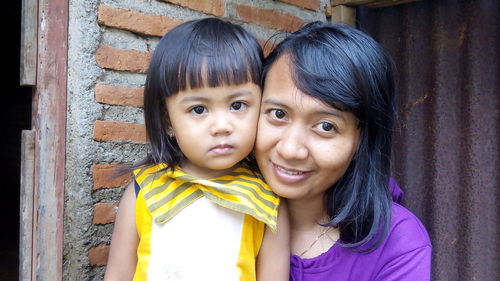 Portrait of mother with daughter against brick wall