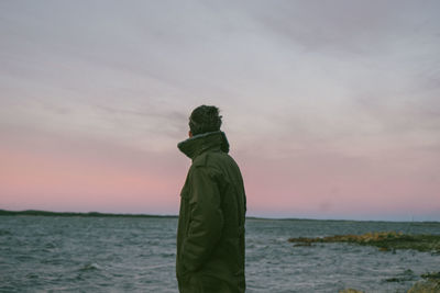 Rear view of man standing by sea against sky during sunset