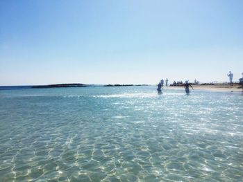 People on beach against clear blue sky