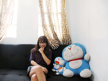 Portrait of young woman smiling while sitting with stuffed toys on sofa at home
