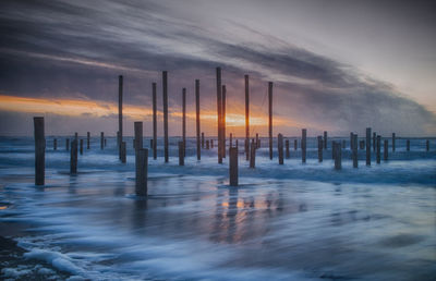 Wooden posts in sea against sky during sunset