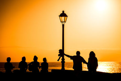 Silhouette people at beach against sky during sunset