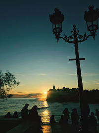 Silhouette people by sea against sky during sunset