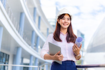 Portrait of a smiling young woman standing against railing