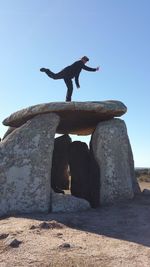 Low angle view of man standing on rock against sky