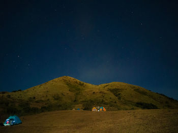 People on field by mountain against sky at night