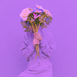 Woman wearing cap holding flowers against colored background