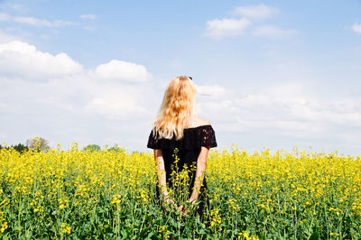 Rear view of woman with hands behind back standing on field