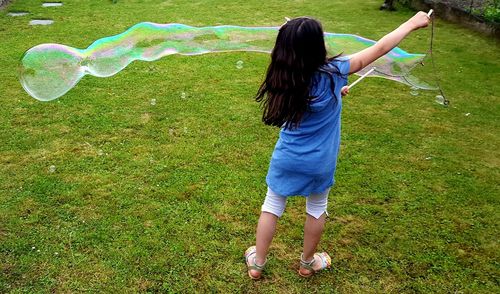 Rear view full length of girl playing with bubble on grassy field