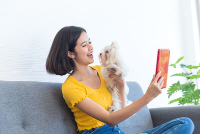 Young woman with dog sitting against white wall