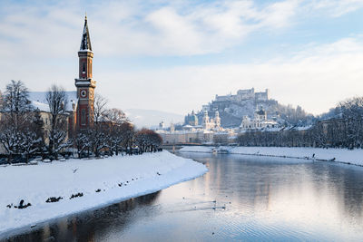 River by town against cloudy sky during winter