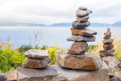 Stack of stones on rock by lake against sky