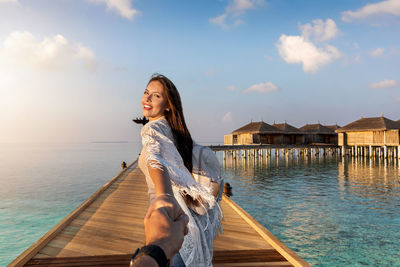 Cropped image of man holding woman hands on pier over sea