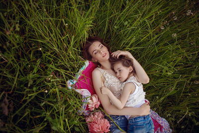 Mother and daughter lie on a green field in summer and relax in the sun