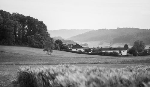 Houses on field by trees against sky