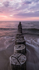 Scenic view of wooden posts in sea at sunset