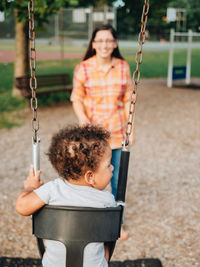 Portrait of smiling woman sitting on swing at playground