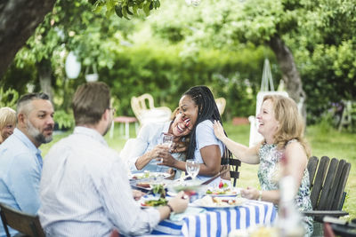 Friends enjoying and having fun while sitting at dining table in garden during summer weekend