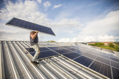 Man carrying solar panel, installing on roof.