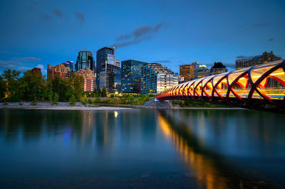 Bridge over river by illuminated buildings against sky