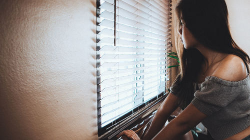 Woman looking away by blinds and window at home