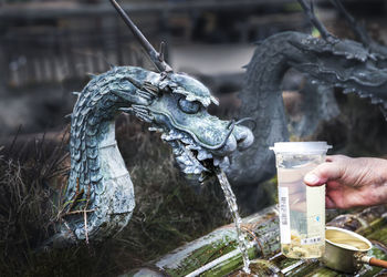 Close-up of hand holding plastic glass in front of dragon fountain