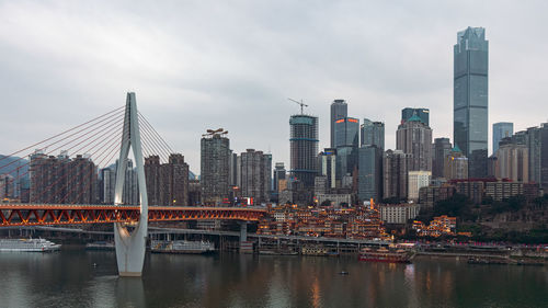 Bridge over river by buildings against sky in city