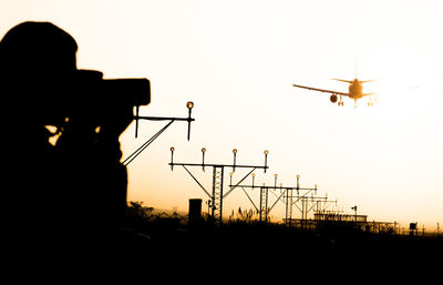 Silhouette man photographing airplane against sky during sunset