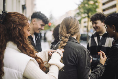 Teenage girl braiding hair of female friend standing at street