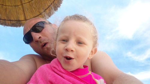 Portrait of father and daughter in swimming pool against sky