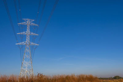 Electric pole and electric cable on the field in the countryside with blue sky.