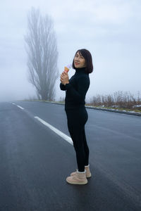 Portrait of young woman standing on road against sky