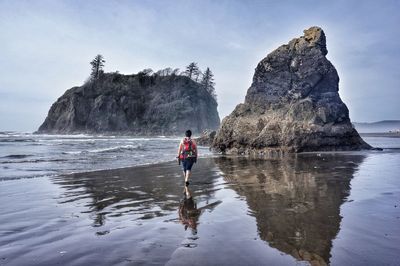 Rear view of woman with backpack walking in sea against sky