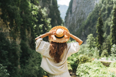 Young woman traveler with long blonde hair in straw hat looks at beautiful view of the mountains