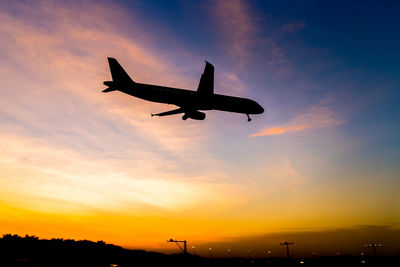 Low angle view of silhouette airplane flying against sky during sunset