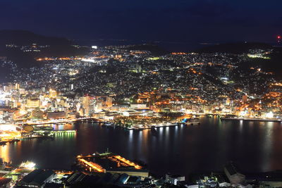 Illuminated cityscape by sea against sky at night