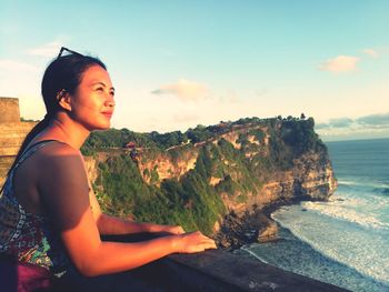 Side view of young woman standing on rock by sea against sky