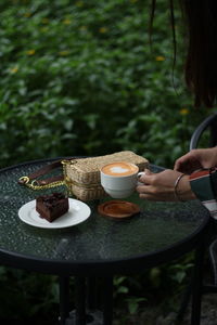 Hand holding coffee cup and saucer on table