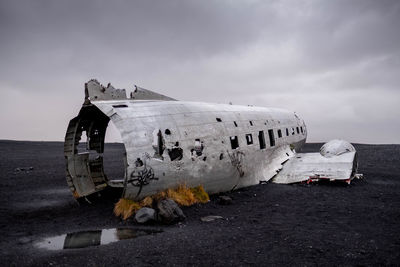 Abandoned airplane at beach against cloudy sky