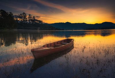 Boat moored in lake against sky during sunset