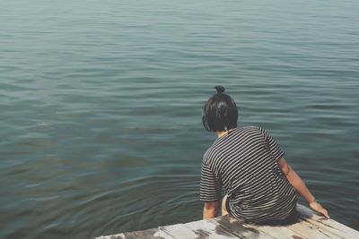 Rear view of woman sitting on jetty in sea