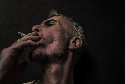 Close-up of man smoking cigarette against black background