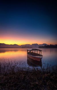 Boat moored in lake against sky during sunset