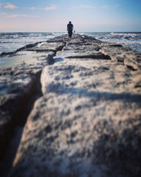 Man walking on rock by sea against sky